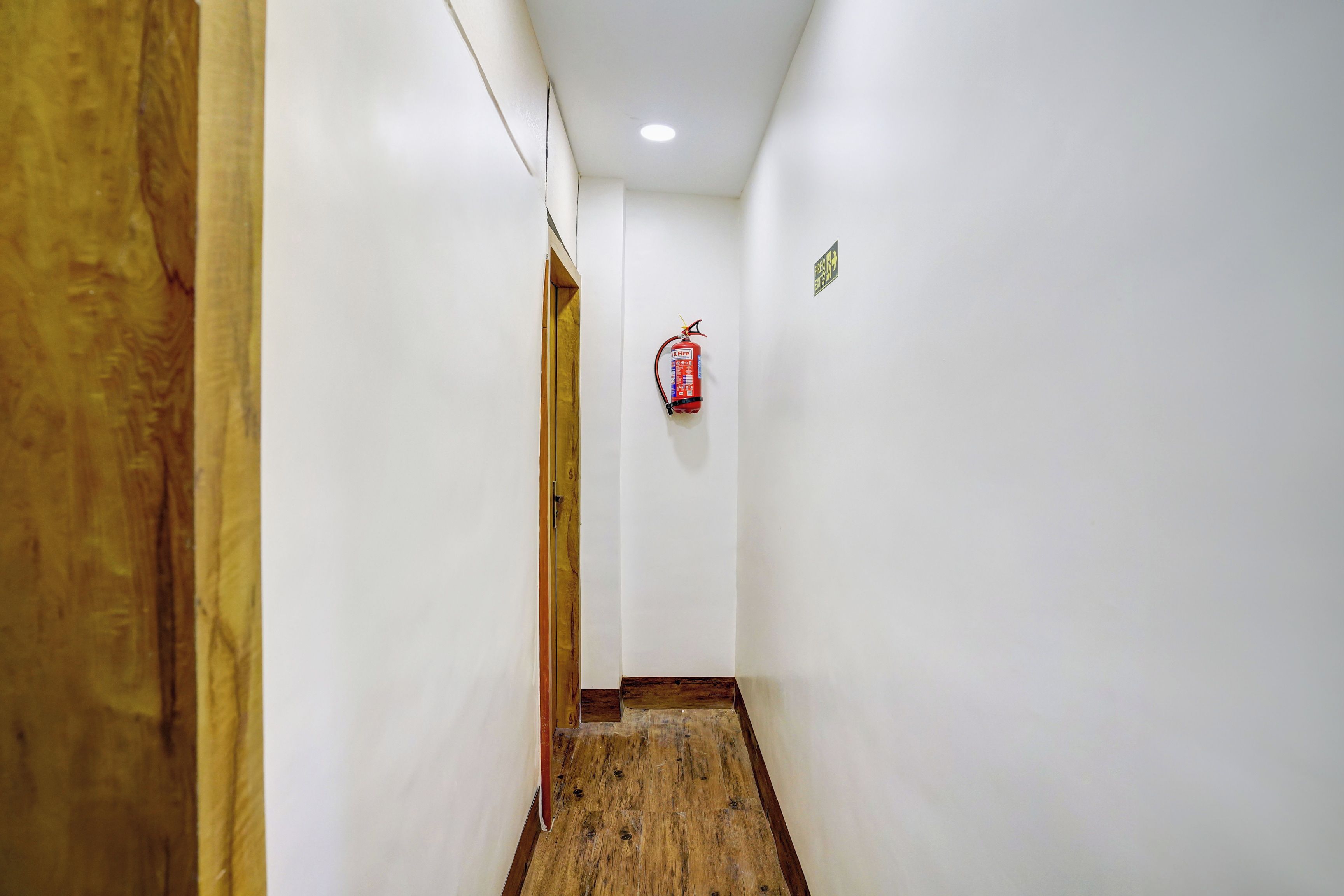 A narrow hallway with white walls, a wooden door frame, and a fire extinguisher mounted on the wall.