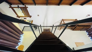 Una escalera con barandilla, vigas de madera y pared blanca.
