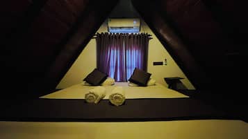 A triangular room with a bed, two pillows, a small table, and an air conditioning unit.
