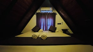 A triangular room with a bed, two pillows, a small table, and an air conditioning unit. - Divine Eco Resort Sigiriya (Sigiriya)