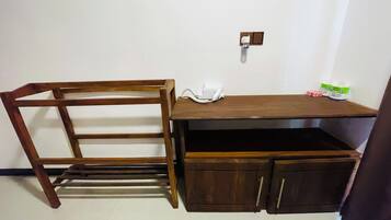 A wooden desk with a chair, a white phone, and a small shelf with items.