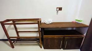 Un escritorio de madera con una silla, un teléfono blanco y una pequeña estantería con objetos.