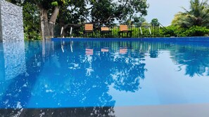Una piscina azul cristalina con sillas de madera y un muro de piedra.