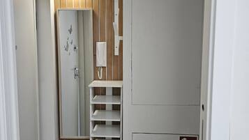A hallway with a white door, a wooden panel wall, a white shelf unit, and a fire safety sign.