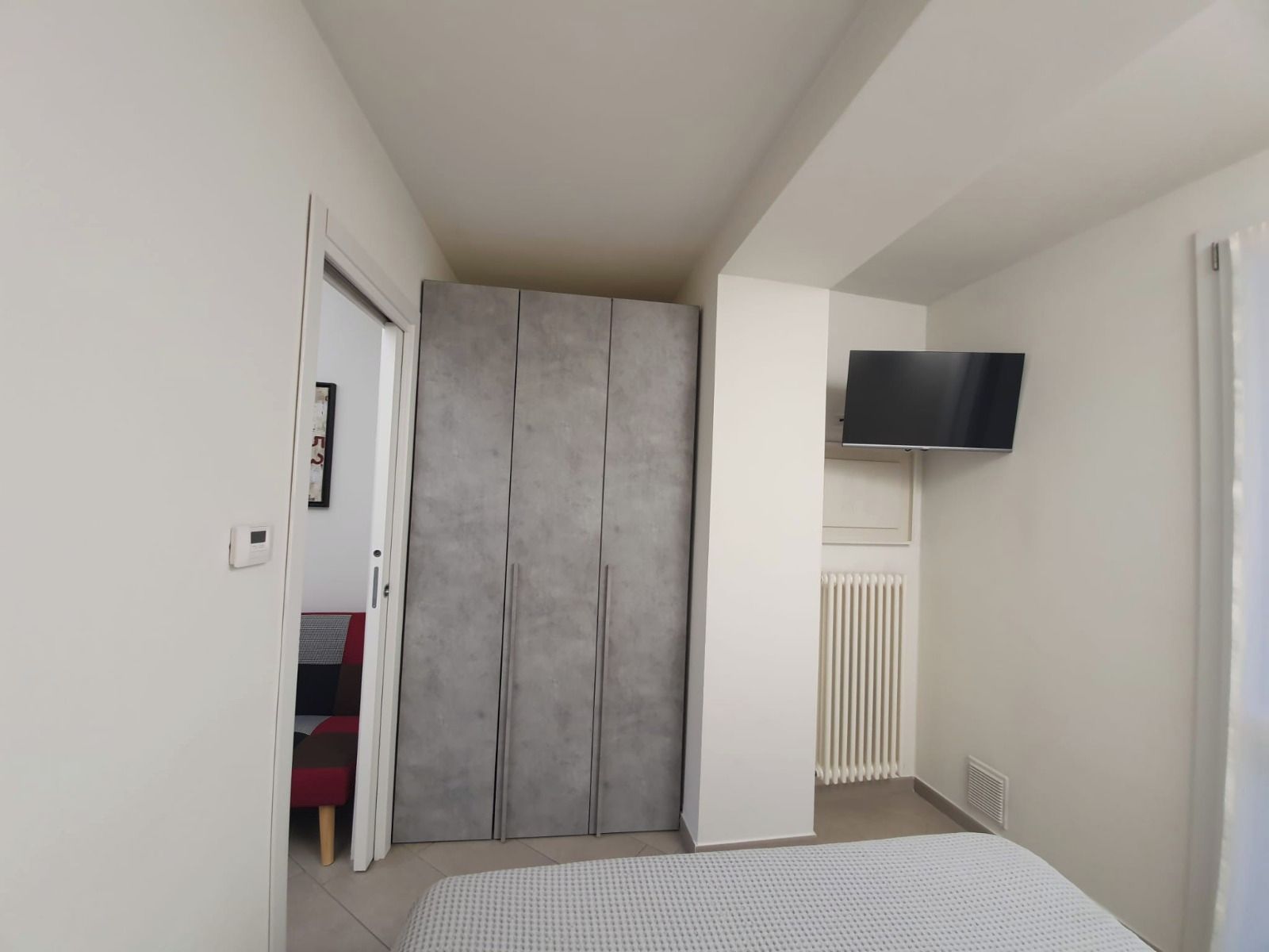 Un dormitorio con cama, armario, televisor y radiador.