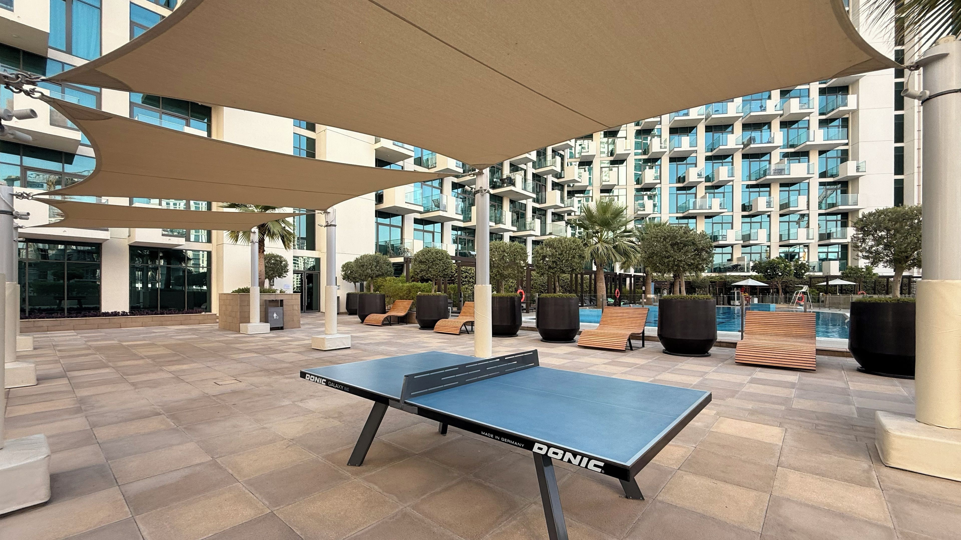Una mesa de ping pong en un espacio exterior con asientos y una piscina.