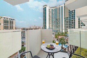 A balcony with a table, chairs, a plate of fruit, and a glass of orange juice. - Azizi Signature Studio Al Jaddaf (Dubai)