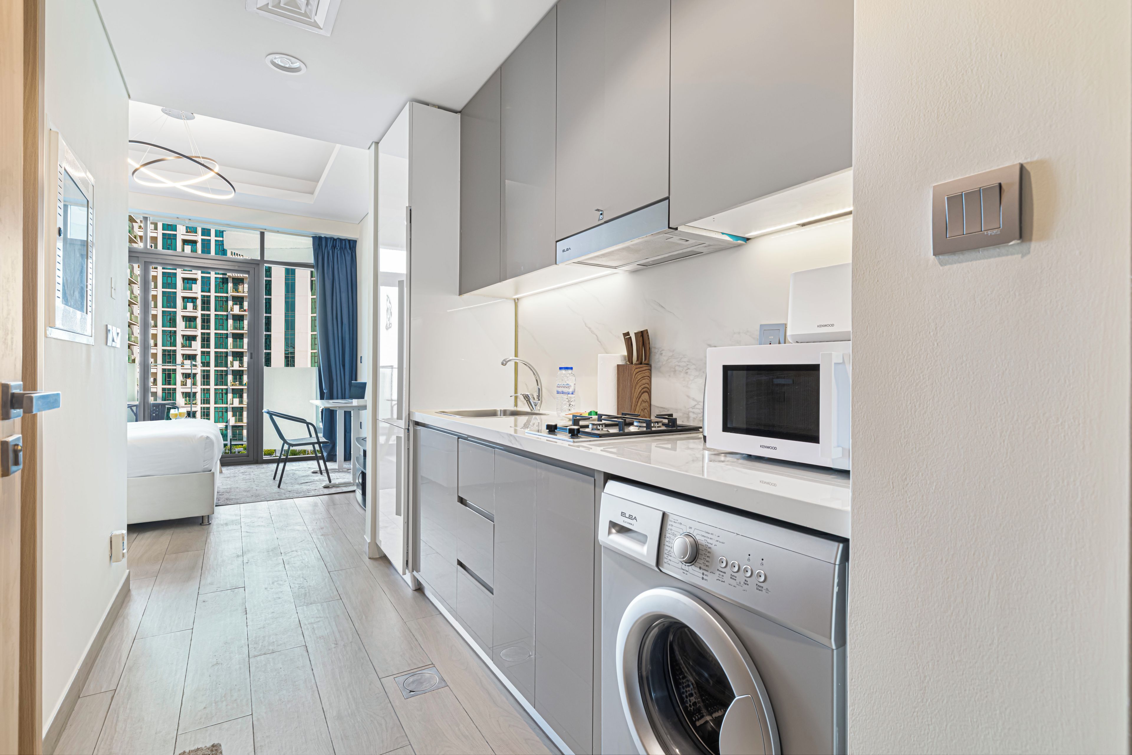A modern kitchen with a built-in washer, a microwave, and a dining area with a view of the city.