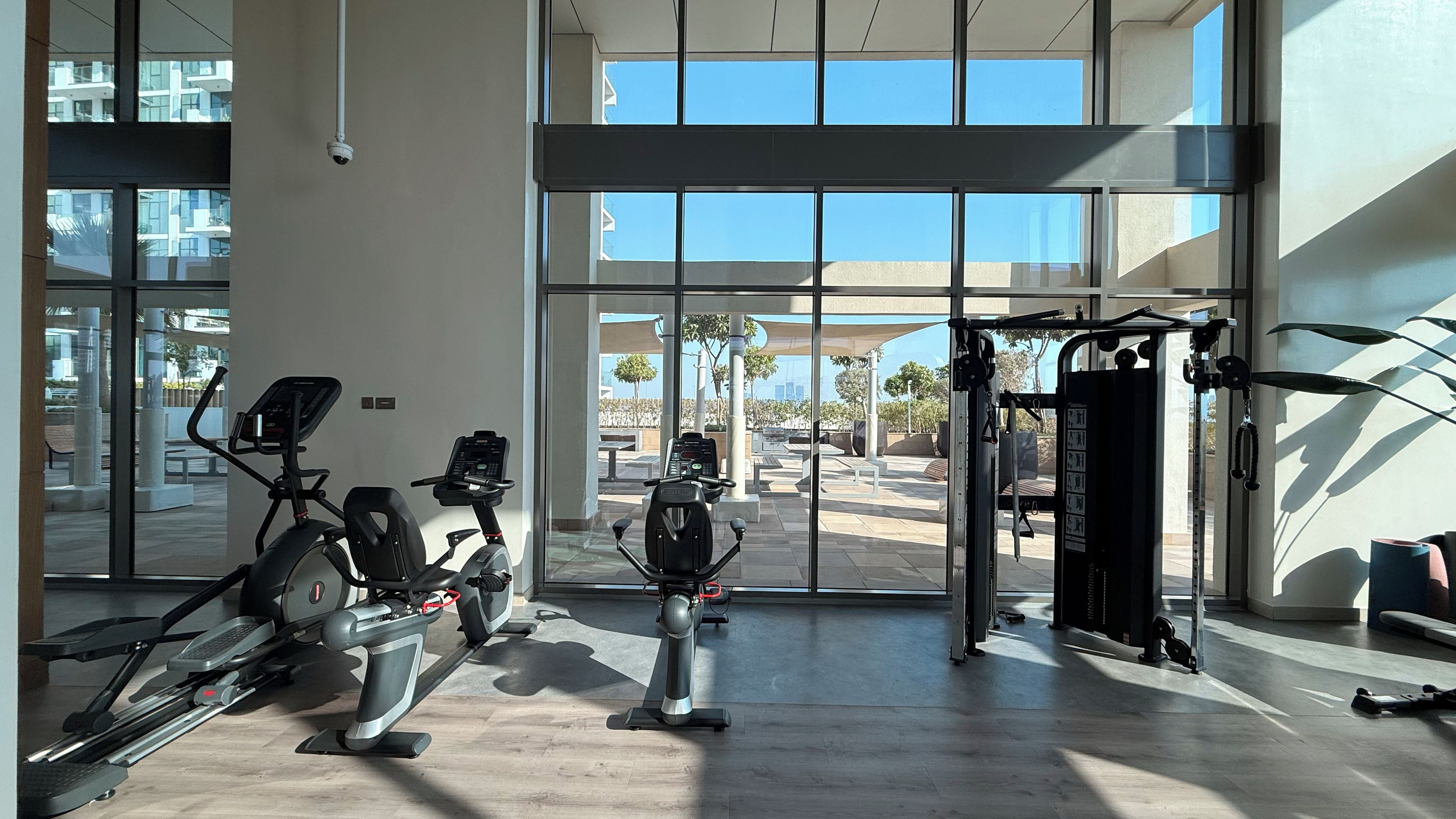 A gym with cardio machines, weightlifting equipment, and large windows offering a view of the outdoors.