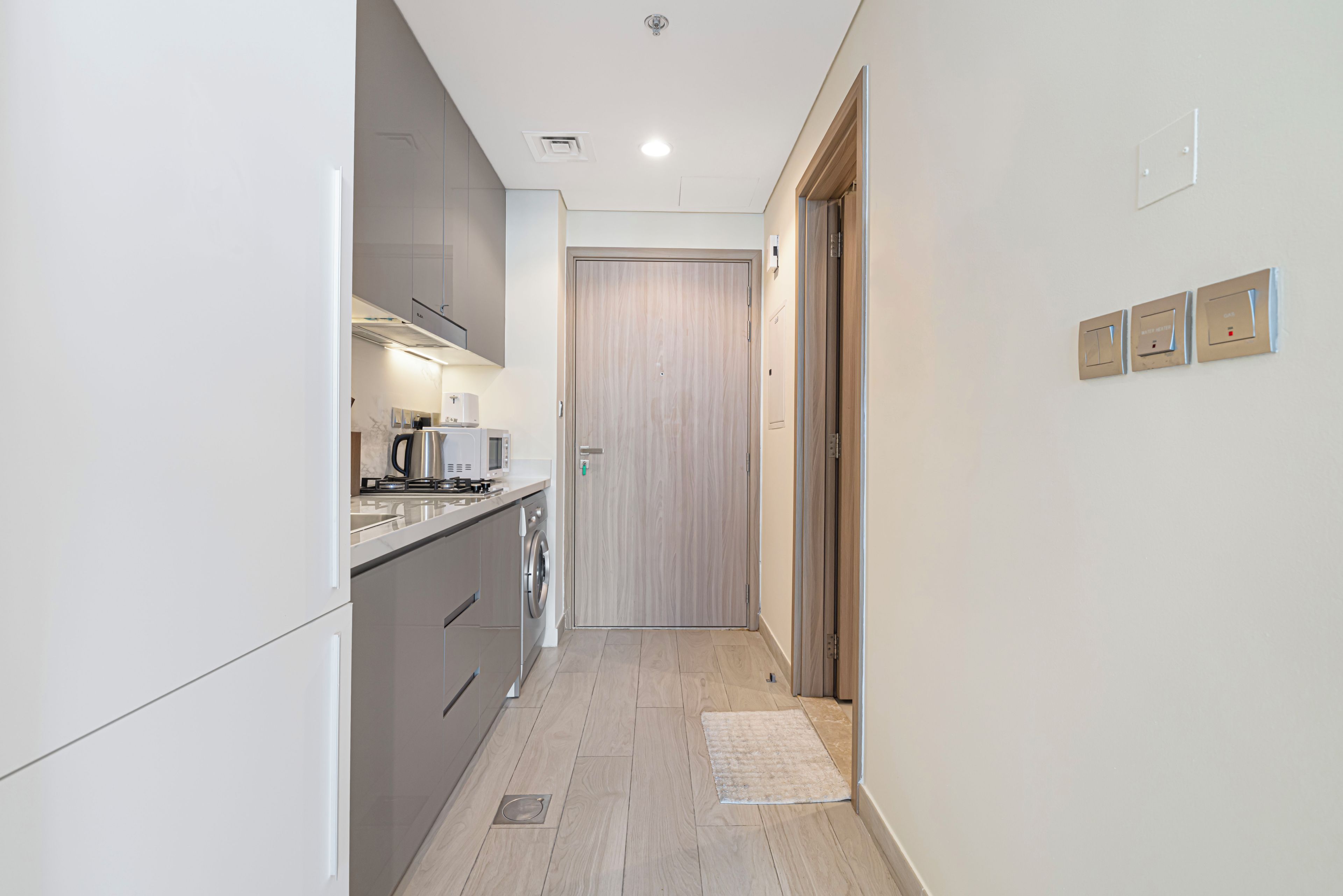 Un couloir étroit mène à une cuisine équipée d’appareils modernes et dotée d’une porte en bois.