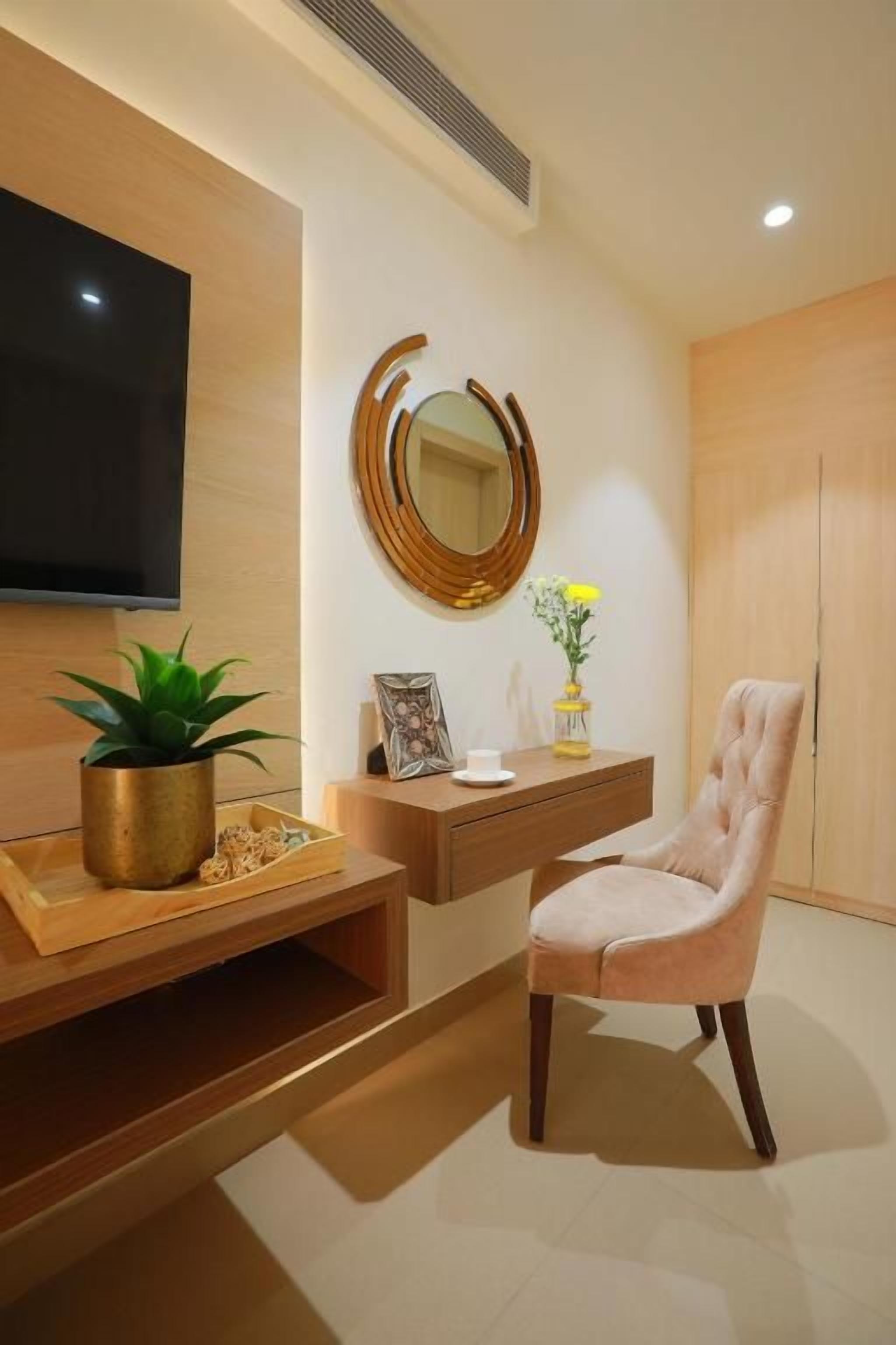 Una sala de estar moderna con un televisor de pantalla plana, un espejo redondo, un aparador de madera, un sillón con cojines y una planta en maceta.