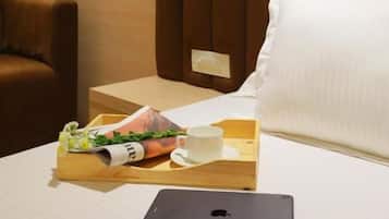 A hotel room with a bed, a bedside table with a tray of breakfast items, a laptop, and a brown leather chair.