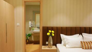 A hotel room with a bed, a bedside table with a vase of flowers, a wooden wardrobe, and a bathroom visible through an open door.