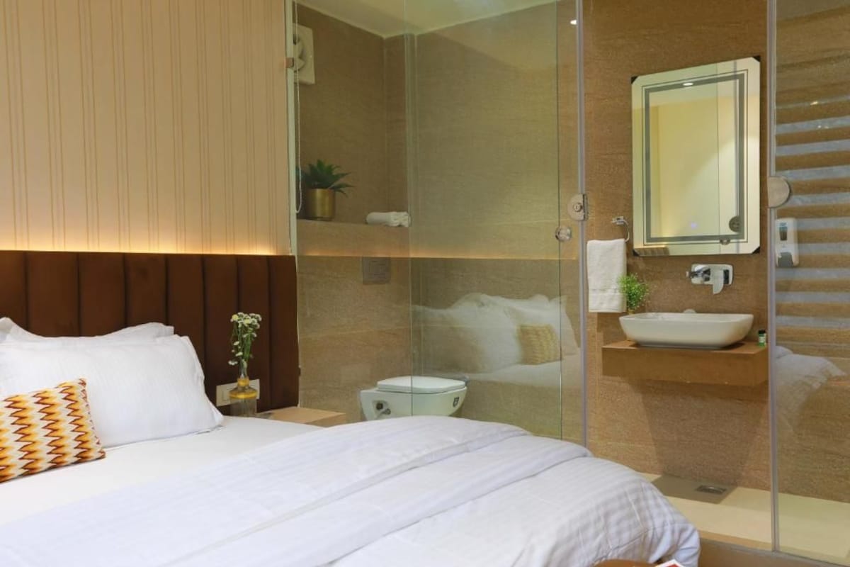 Ein modernes Hotelzimmer mit einem großen Bett, einer Duschkabine aus Glas, einem integrierten Waschbecken und einem Spiegel darüber.