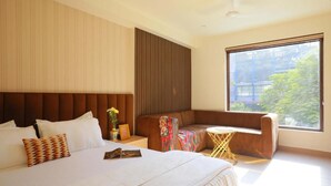Et moderne hotelværelse med en stor seng, en sofa, et lille rundt bord og et stort vindue med udsigt til grøn natur.