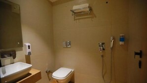 A bathroom with a toilet, a sink, a mirror, a towel rack, and a shower. - Hotel Adora (New Delhi)