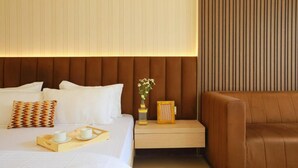 A hotel room with a bed, bedside table, and a brown leather sofa. - Hotel Adora (New Delhi)