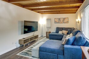 Ein modernes Wohnzimmer mit einer Eckcouch, einem flachbildfernseher an der Wand und einer Holzbalkendecke.