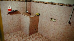 A bathroom with a tiled floor, a shower area, and a shelf with toiletries. - HST Coffee and Homestay Wonosobo (Wonosobo)