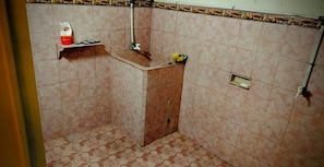 Casa de banho com chão em azulejos, zona de duche e prateleira com artigos de higiene pessoal.