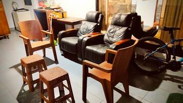A living area with a massage chair, a dining table, wicker chairs, and a bicycle.