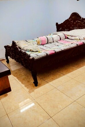 A bed with a patterned bedspread and pillows, a wooden headboard, and a tiled floor.