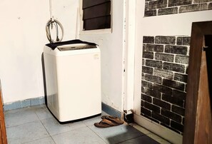 A compact white appliance, possibly a refrigerator, in a corner with a tiled floor and a small window. - HST Coffee and Homestay Wonosobo (Wonosobo)