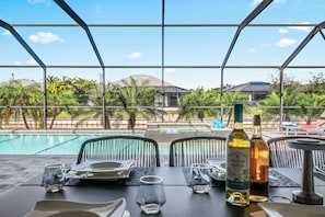 Un espace repas avec vue sur une piscine, des sièges d’extérieur et une table dressée pour deux personnes.