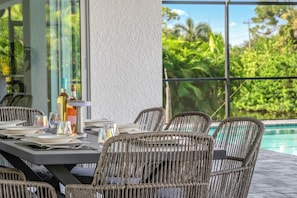 Un espace extérieur aménagé pour les repas, avec des chaises en osier et une table dressée, offrant une vue sur une piscine et une végétation luxuriante.