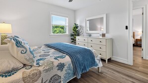 A bedroom with a bed, a dresser, a ceiling fan, a window, and a door leading to another room. - Kayak + Fishing Dock | Pool + Spa | Mangroves + Beaches | Sanctuary Point (Bonita Springs)