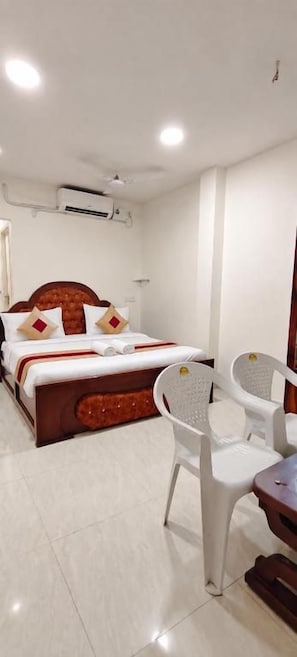 A hotel room with a bed, a chair, a table, and an air conditioning unit. - Roja Palace (Mahabalipuram)