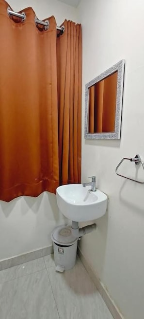 A bathroom with a white sink, a mirror, and a toilet. - Roja Palace (Mahabalipuram)