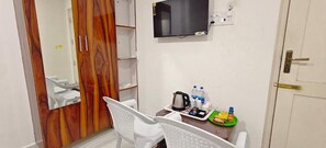 A hotel room with a wooden wardrobe, a television mounted on the wall, a small table with a kettle, cups, and a tray with snacks.