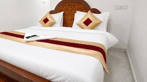 A neatly made bed with a wooden headboard, white bedding, and a red and beige bedspread. - Roja Palace (Mahabalipuram)
