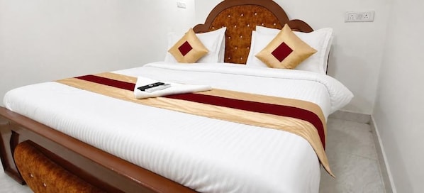 Una cama bien hecha con cabecera de madera, ropa de cama blanca y una colcha beige y roja.