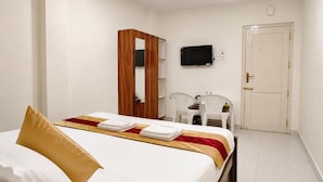 A hotel room with a bed, a TV, a wardrobe, and a desk with chairs. - Roja Palace (Mahabalipuram)