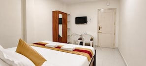 A hotel room with a bed, a TV, a wardrobe, and a desk with chairs. - Roja Palace (Mahabalipuram)