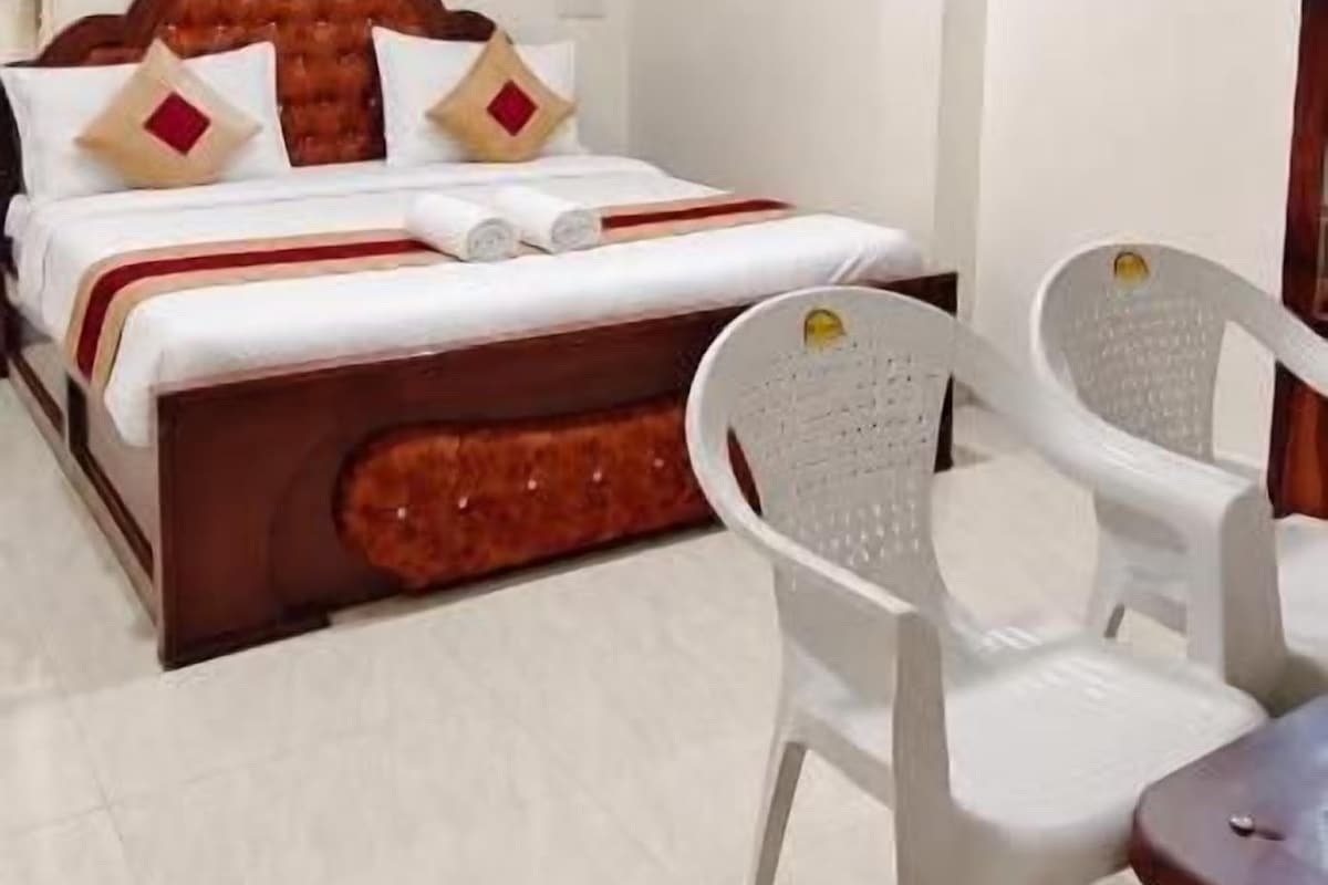 A hotel room with a bed, a chair, a table, and an air conditioning unit.