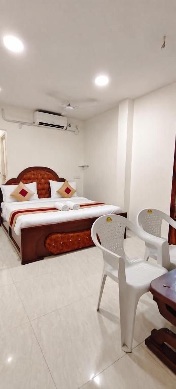 A hotel room with a bed, a chair, a table, and an air conditioning unit.