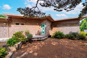 A modern house with a wooden facade, a green door, and a gravel driveway. - Ocean-View Deck + Fire Pit + BBQ | Short Walk to the Beach | The Grey Piper (Arch Cape)