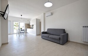 Ein modernes Wohnzimmer mit einem grauen Sofa, einem Essbereich mit Tisch und Stühlen sowie einer Küche im Hintergrund.