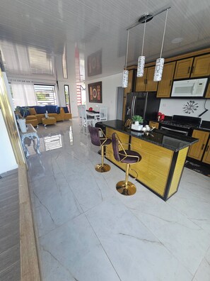 A modern kitchen with a central island, bar stools, and a dining area with a sofa and chairs. - - Bonao Yaneris Luxury Apartament (Bonao)