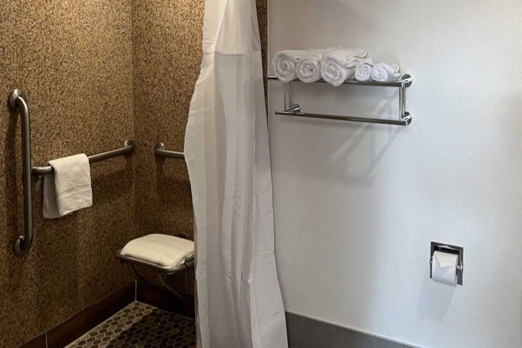 Un baño con inodoro, barra de apoyo, toallero con toallas y cortina de ducha.