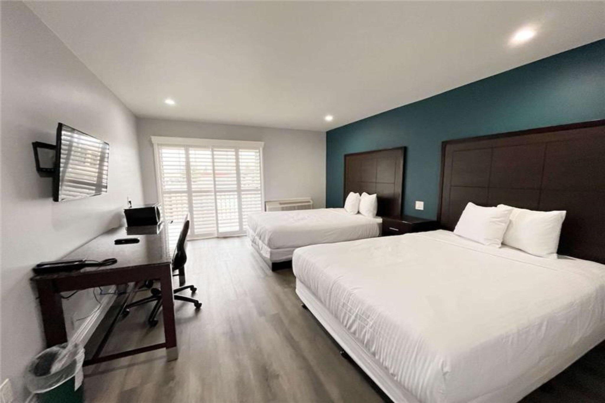 A hotel room with two beds, a desk, and a television.