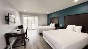 A hotel room with two beds, a desk, and a television.
