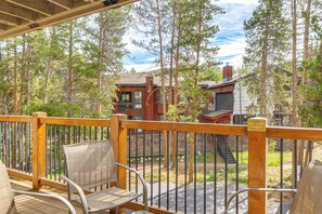 A wooden deck with metal railings, outdoor seating, and a view of forested buildings. - Walk to Ski & Main St! Newly Refinished w/ Hot Tub (Breckenridge)