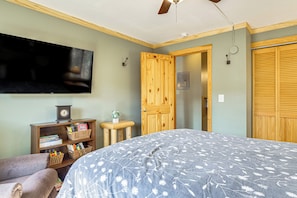 Ein Schlafzimmer mit einem großen Bett, einem an der Wand montierten Fernseher, einem Holzschrank und einem kleinen Tisch mit einer Pflanze.