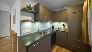 A modern kitchen with dark cabinetry, a stainless steel sink, and a built-in oven. - Suite with private sauna (Gaschurn)