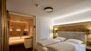A bedroom with a large bed, wooden headboard, and a glass-enclosed walk-in closet. - Suite with private sauna (Gaschurn)