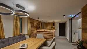 A modern interior with a wooden dining table, grey upholstered chairs, and a wooden accent wall. - Suite with private sauna (Gaschurn)